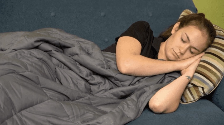 A folded grey weighted blanket for anxiety resting on a bed, showcasing its quilted texture for even pressure distribution.