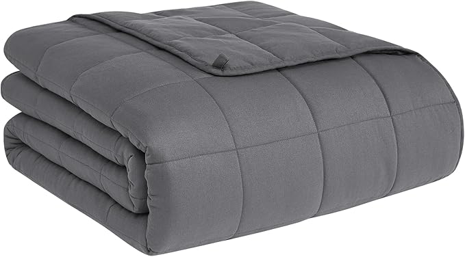 A folded grey weighted blanket for anxiety resting on a bed, showcasing its quilted texture for even pressure distribution.