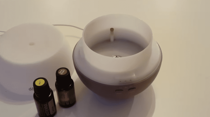 A white and wood grain ultrasonic essential oil diffuser emits a cool mist for a relaxing home atmosphere.